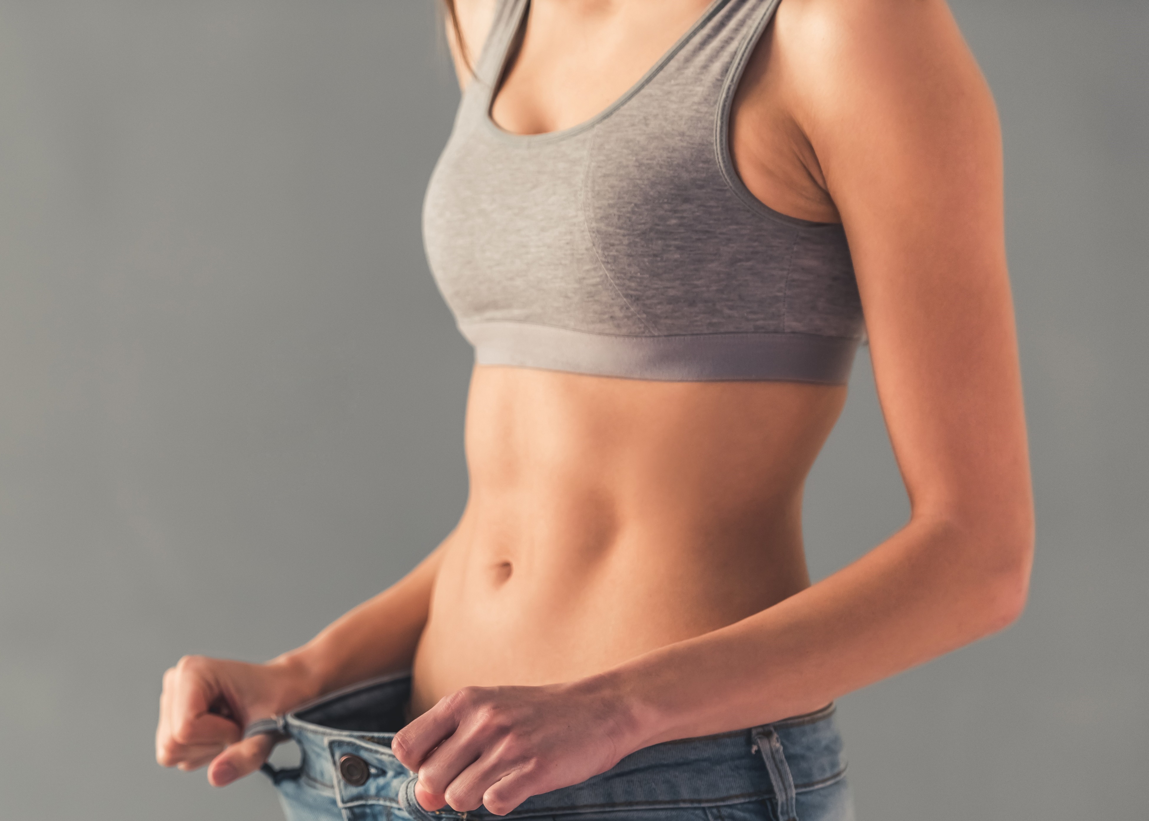 A woman in a sports bra top holding a pair of jeans.