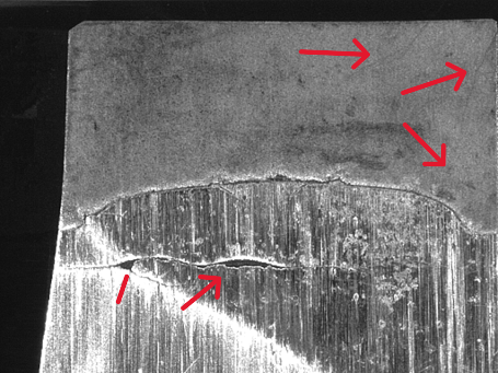 Micrograph of a PDC cutter edge with red arrows marking wear and fracture along the diamond table interface