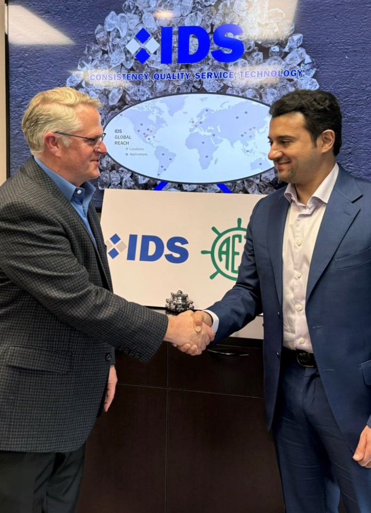 Two IDS representatives shaking hands in front of a branded wall showing the IDS global reach map