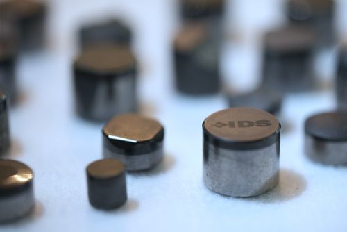 Polished IDS polycrystalline diamond compact cutters arranged on a light surface, one stamped with the IDS logo