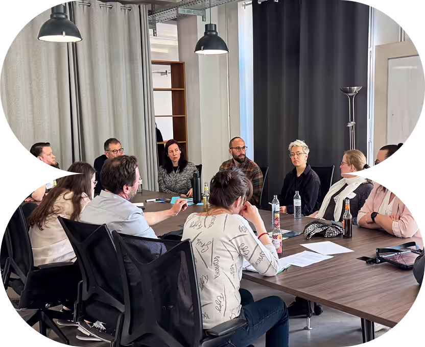 Neun Personen sitzen an einem Konferenztisch in einem modernen Besprechungsraum und führen eine Diskussion.