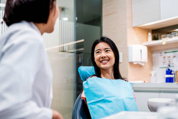 Smiling patient looking at dentist in clinic Smiling mid adult patient looking at healthcare worker. Female is sitting on dentist's chair. They are in dental clinic. asian female at dentist smiling stock pictures, royalty-free photos & images
