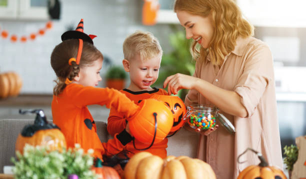 happy Halloween! mother treats children with candy at home happy Halloween! a mother treats children with candy at home Mom and two kids sorting Halloween candy on the kitchen table, laughing together. stock pictures, royalty-free photos & images