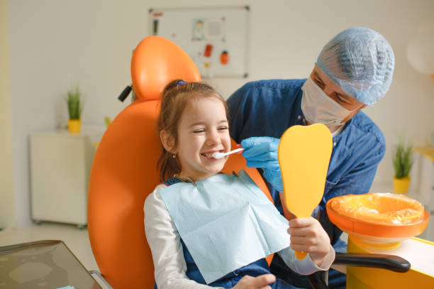 a male dentist teaches a little girl how to brush her teeth properly with a toothbrush a male dentist teaches a little girl how to brush her teeth properly with a toothbrush. Dentist showing a child how to brush properly with a model tooth stock pictures, royalty-free photos & images