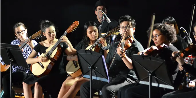 Group of musicians playing guitars and violins on stage with a dark background.