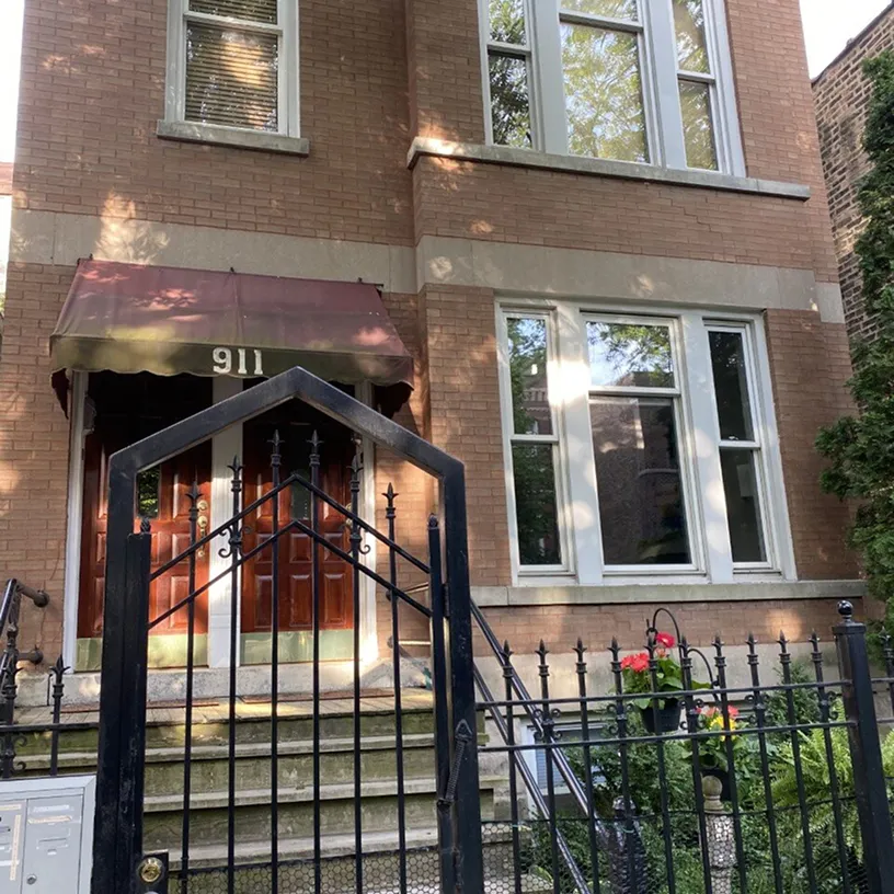 Brick townhouse entrance with a red awning numbered 911, wooden double doors, and a black wrought-iron gate with steps leading up to the door.