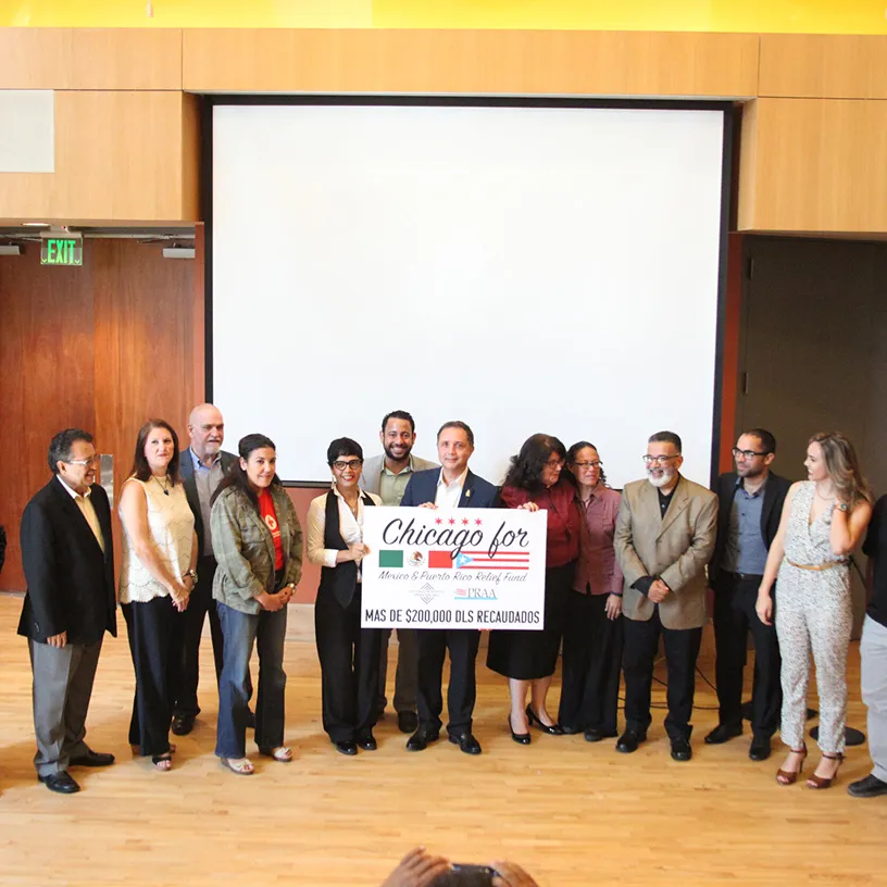 Group of people standing indoors holding a sign that reads 'Chicago for Mexico & Puerto Rico Relief Fund'.