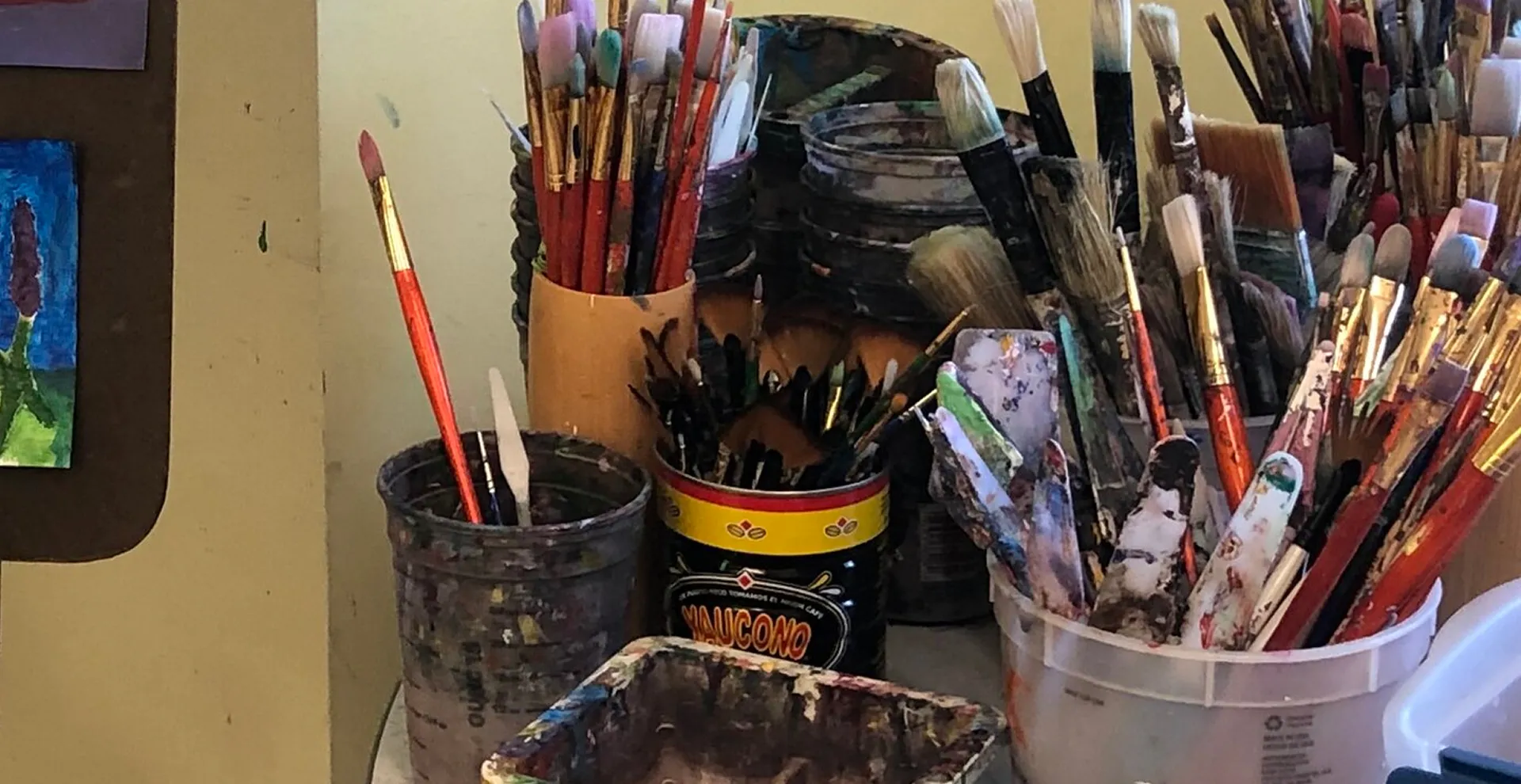 Containers filled with various paintbrushes and palette knives, some covered in paint.