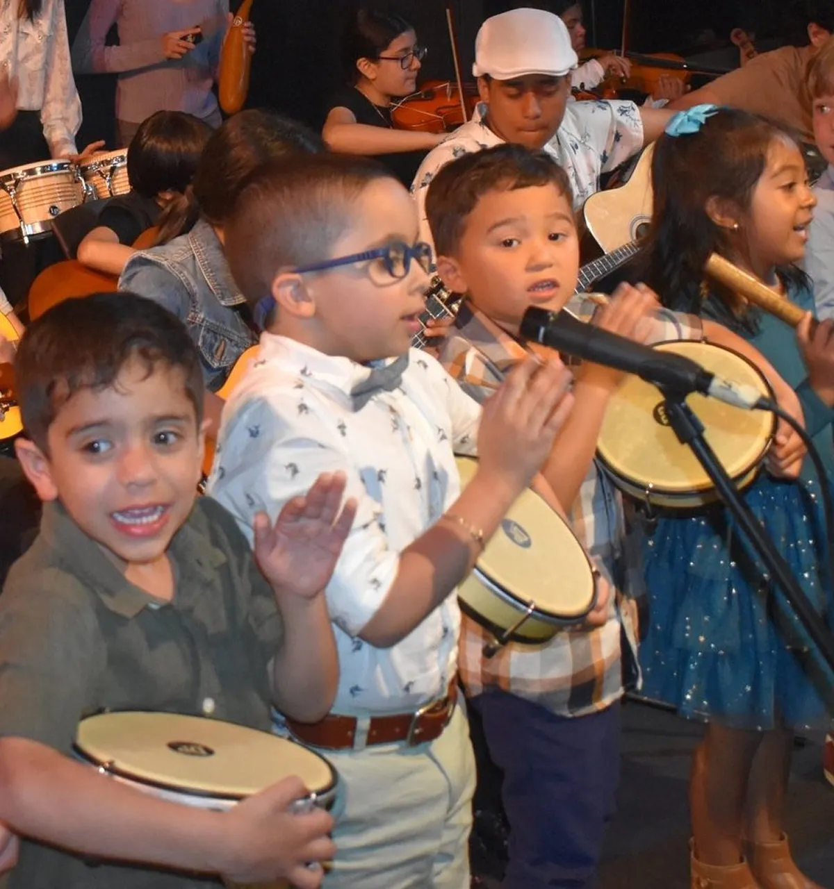 Group of young children playing percussion instruments and singing in a music performance.