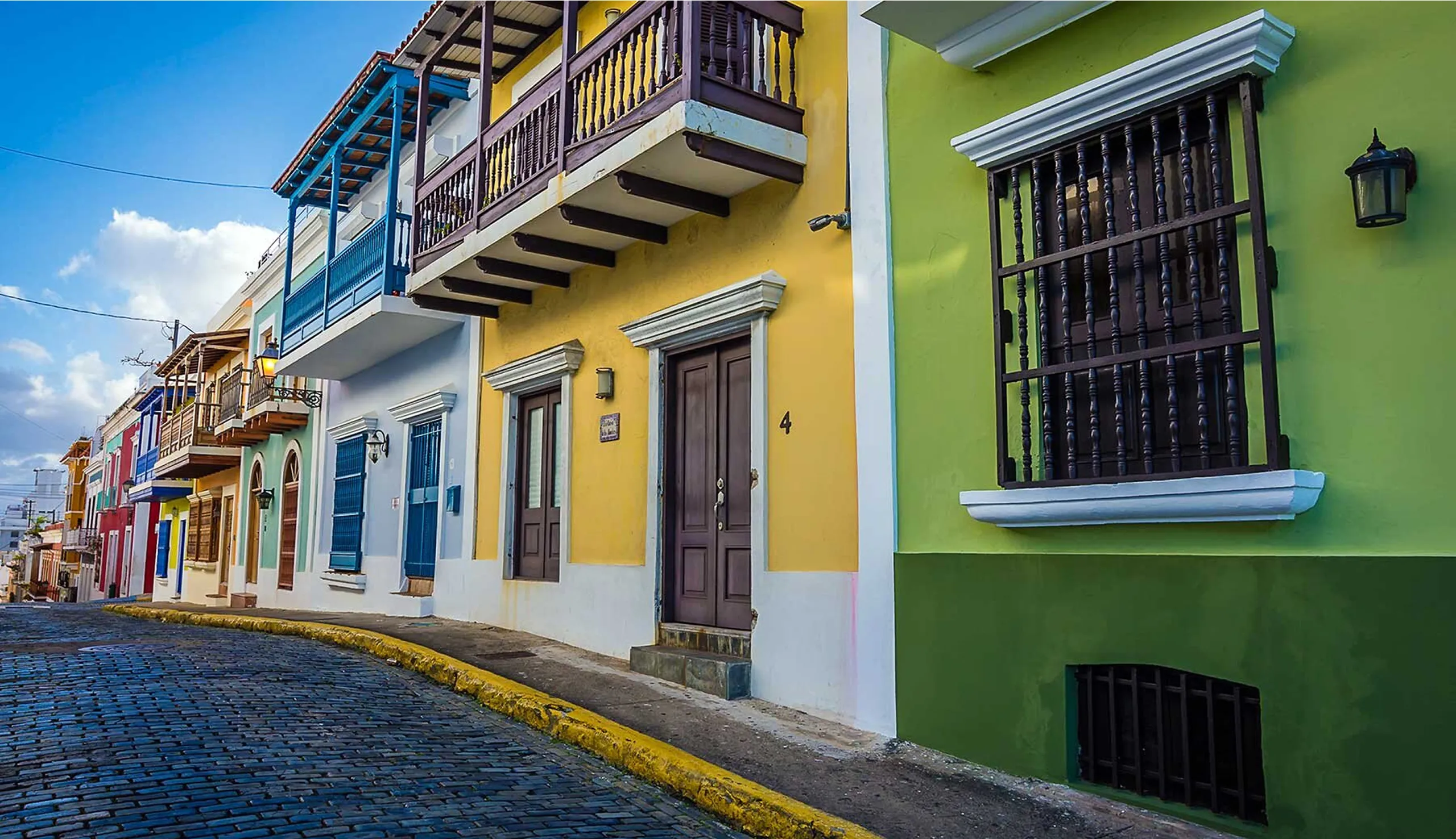 Colorful Spanish colonial buildings with balconies line a cobblestone street in Old San Juan, Puerto Rico, under a bright blue sky.