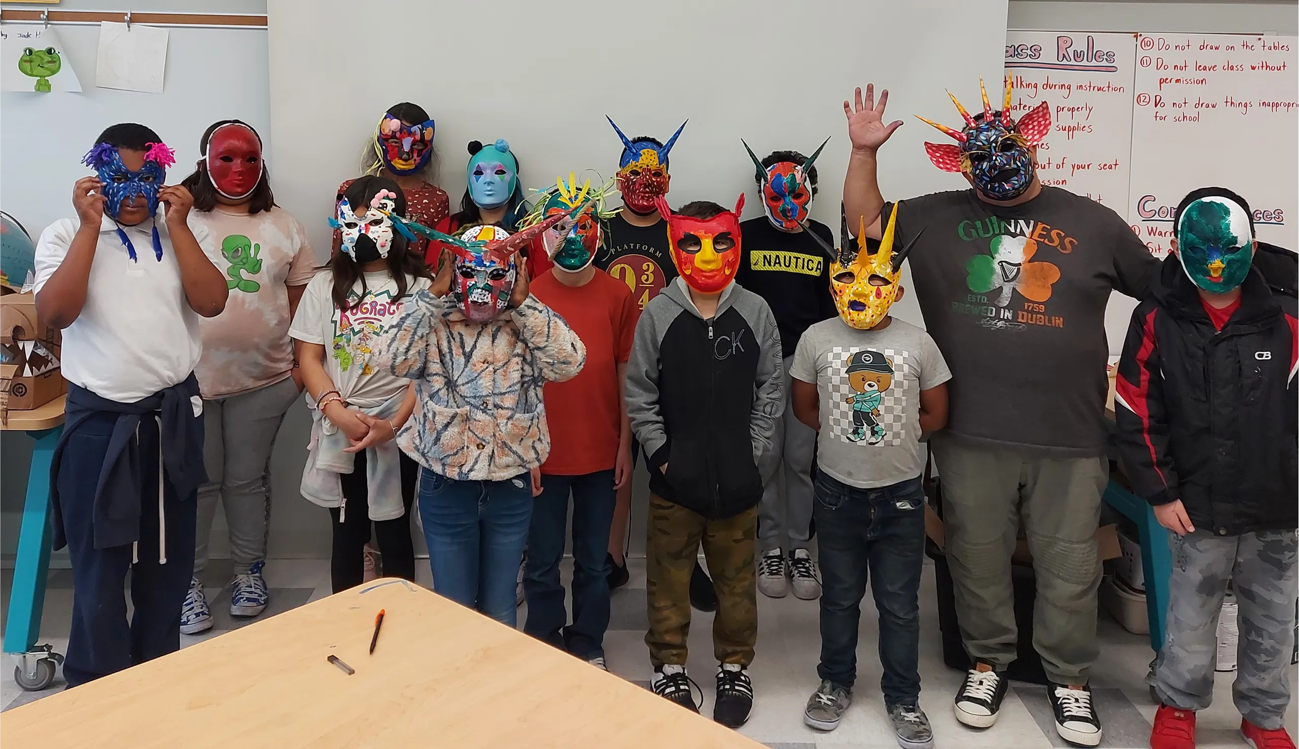 Group of children and one adult wearing colorful, decorated masks standing in a classroom.