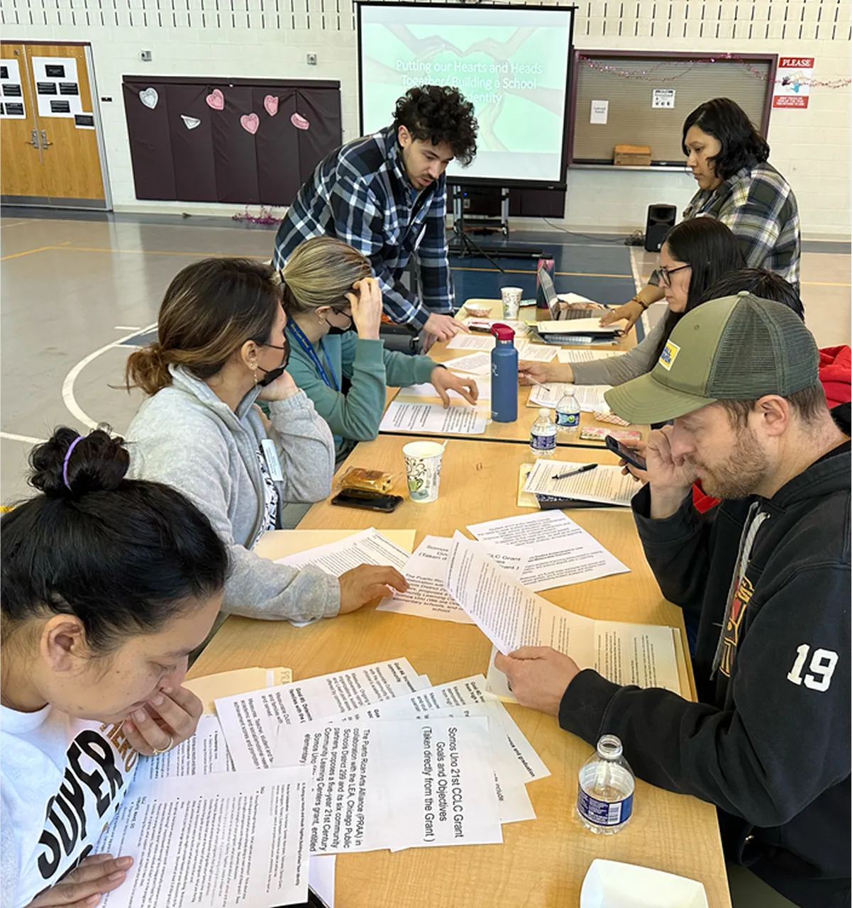 Group of adults seated around a table in a gymnasium, reviewing papers and discussing.
