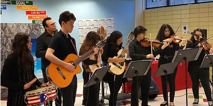 Group of young musicians playing guitar, violin, and drums during an indoor performance.