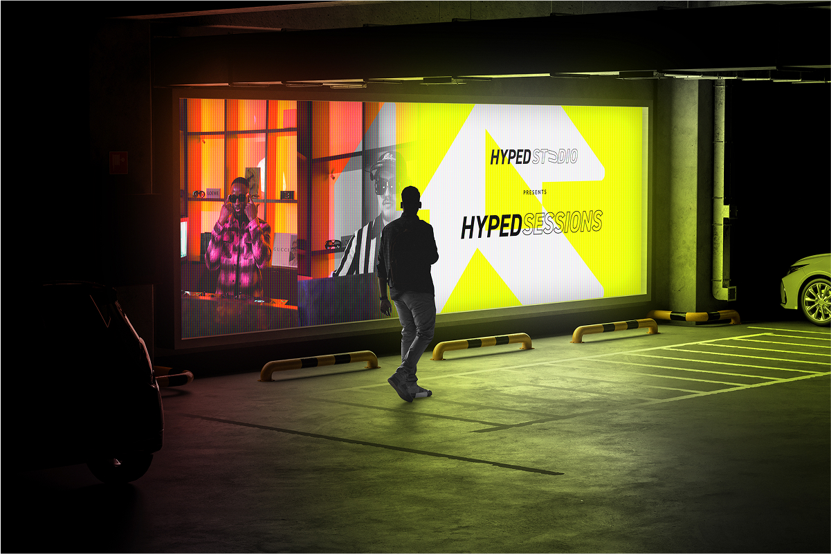 Person standing in a dimly lit parking garage looking at a large illuminated sign that reads 'HYPED STUDIO presents HYPED SESSIONS'.