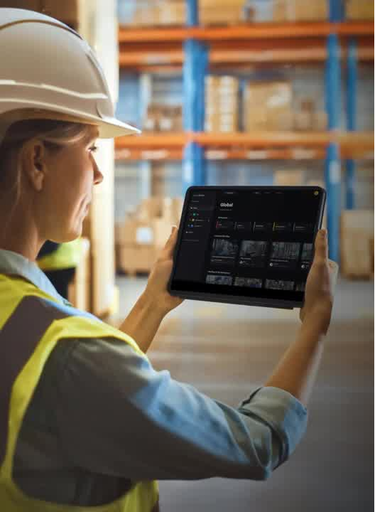 A woman wearing a hard hat and a yellow vest holding a tablet.