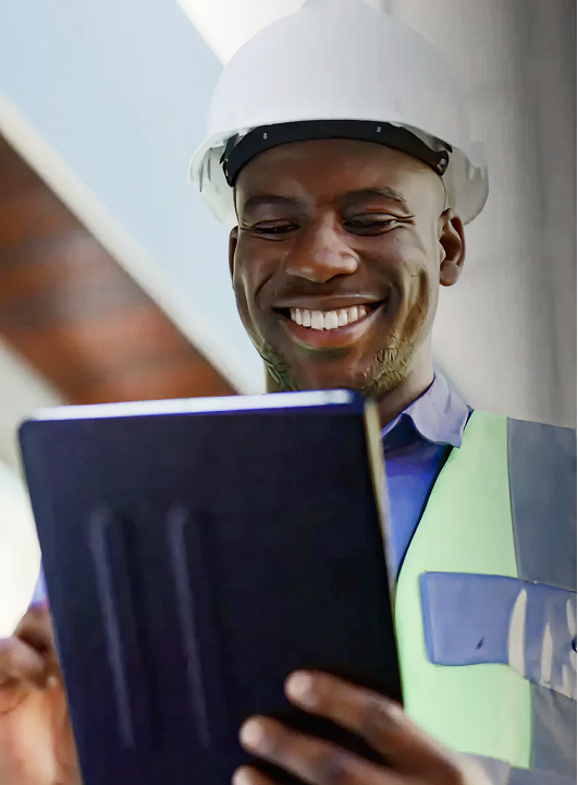 A man wearing a hard hat and a blue shirt is holding a tablet.