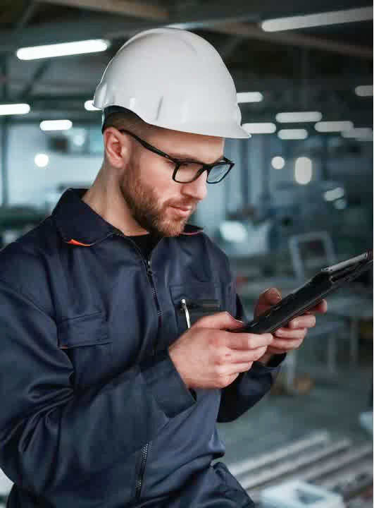 A man wearing a hard hat is looking at a tablet.