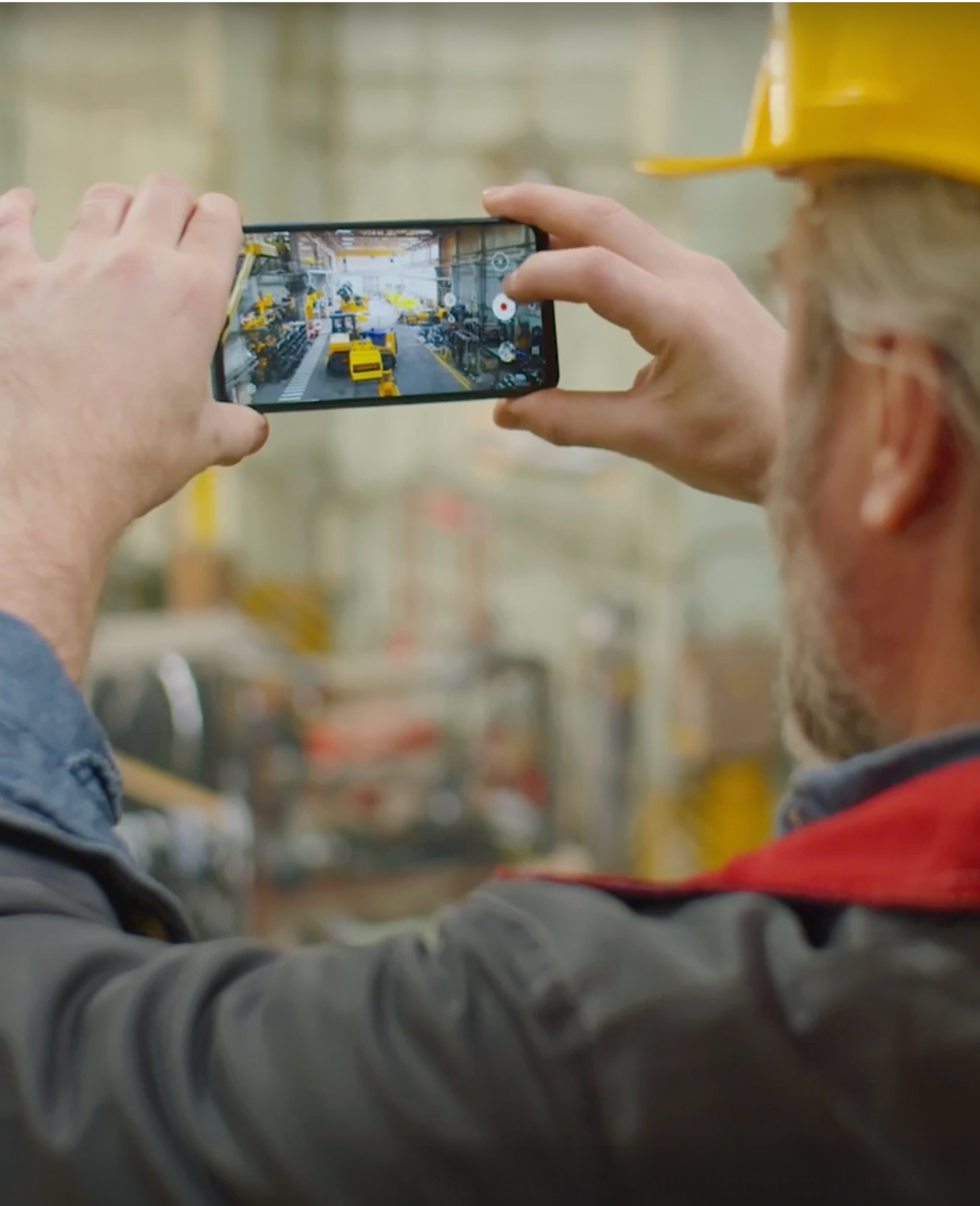 A man wearing a yellow hard hat is taking a picture of a factory.