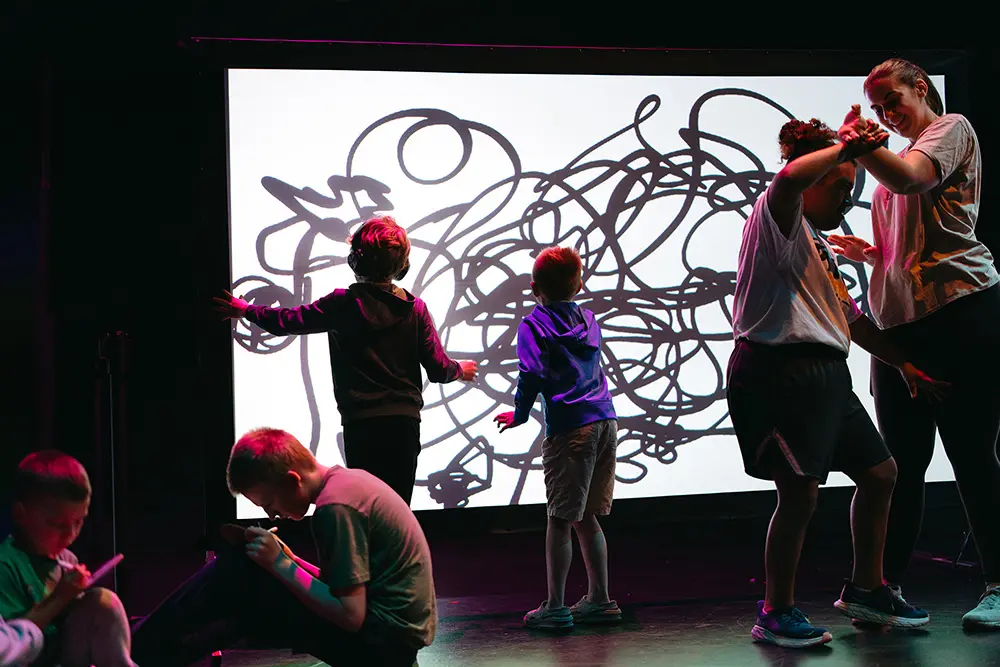 Two children looking at wall art. Two in front of them sitting down. Two other people to their right dancing.
