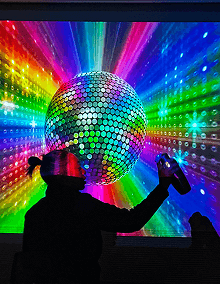 Black silhouette of someone in front of a large disco ball. The background is rainbow colors.