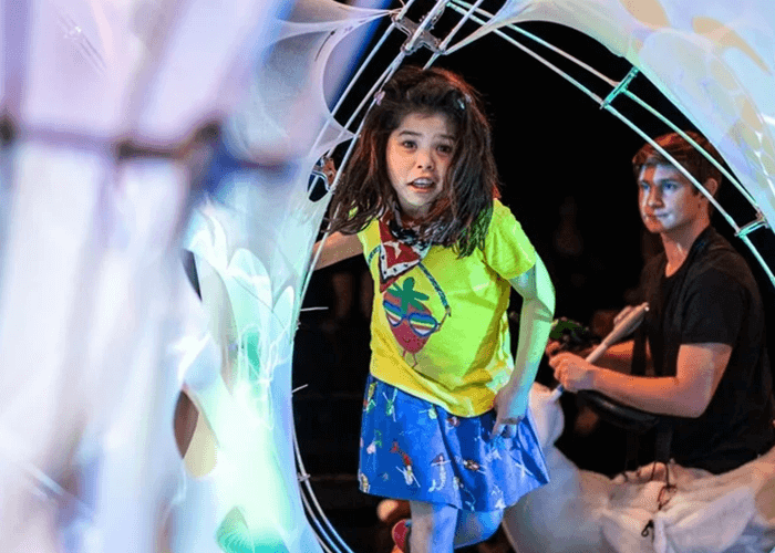 A young girl inside an art piece. An adult knees behind her.