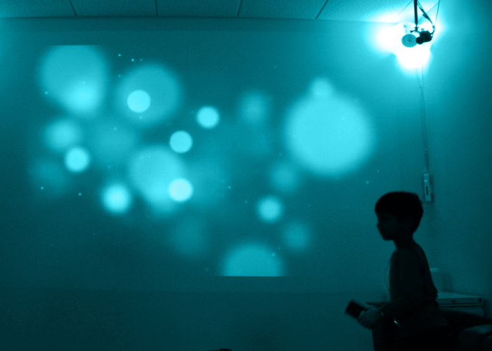 Black silhouette of a young boy in a room, covered in teal light.