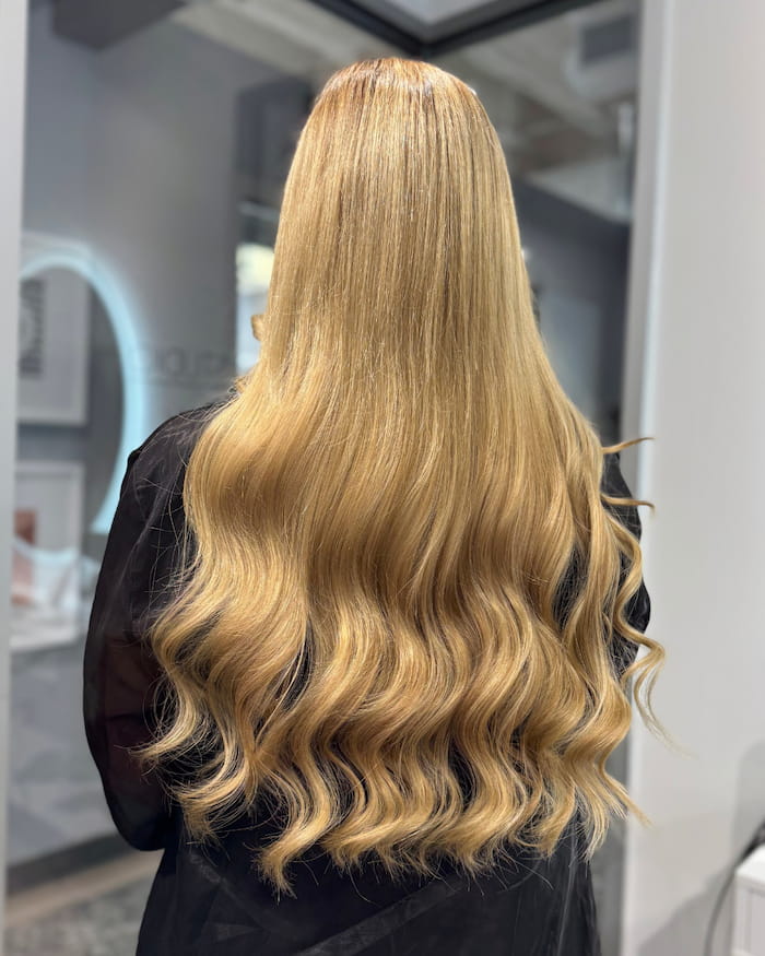 Back view of voluminous blonde Ice Fusion hair extensions with natural waves by Bloom Studio Hair Extensions in Houston