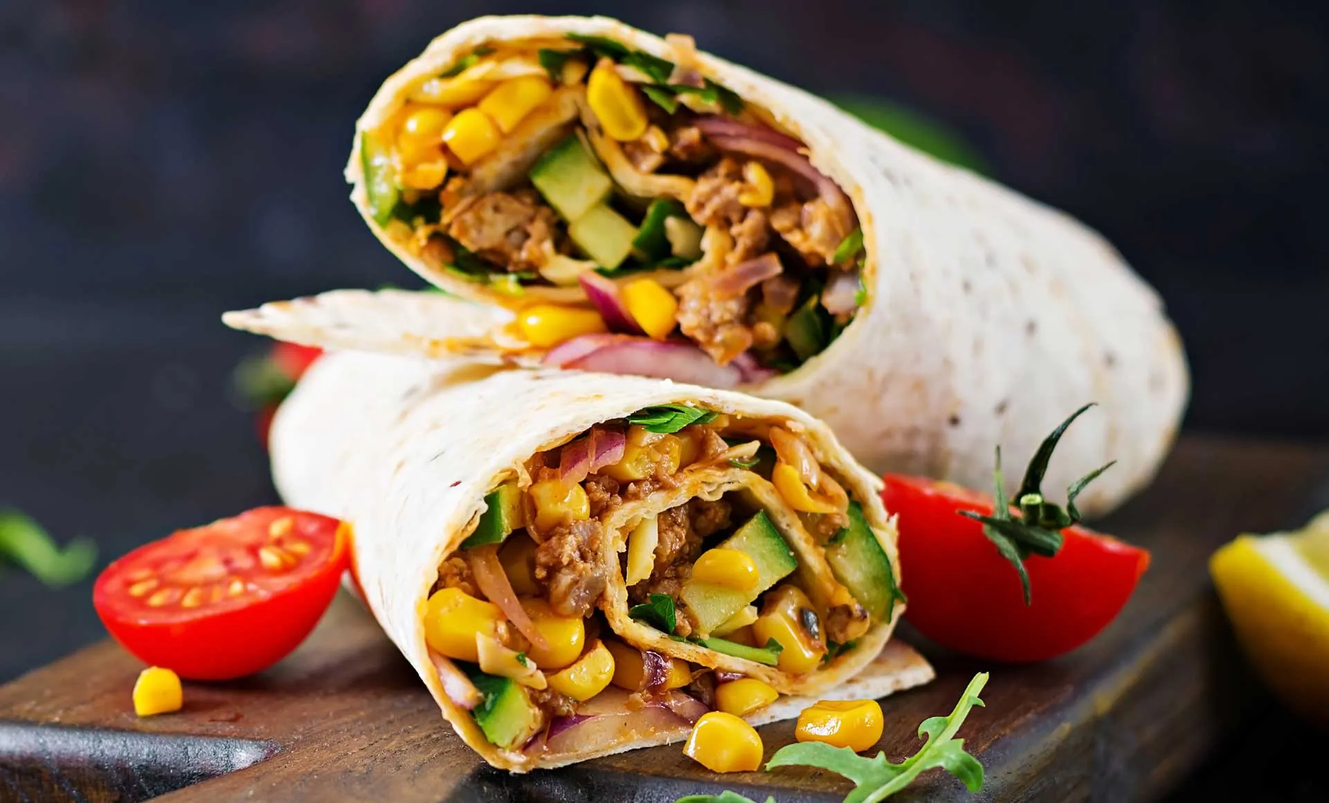 A wrap filled with seasoned meat, fresh vegetables, and ripe tomatoes, neatly rolled for easy eating.