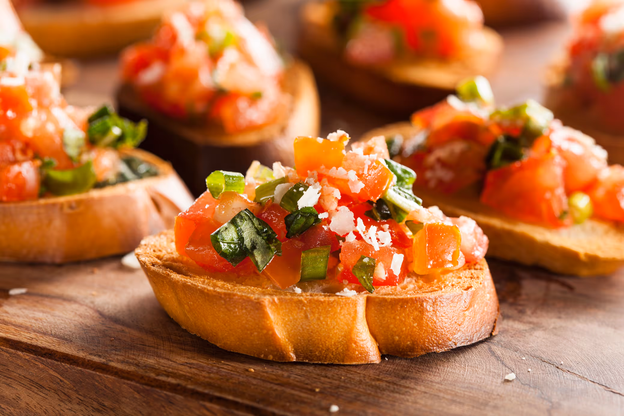 Close-up of vibrant bruschetta on toasted bread, topped with diced tomatoes, basil, and Parmesan cheese. The warm, fresh tones evoke a savory and inviting atmosphere.