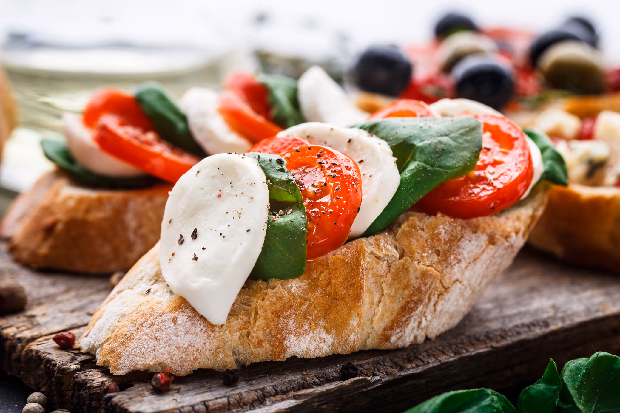Close-up of a fresh bruschetta with sliced mozzarella, tomatoes, and basil on a rustic wooden board. The scene is vibrant and appetizing.