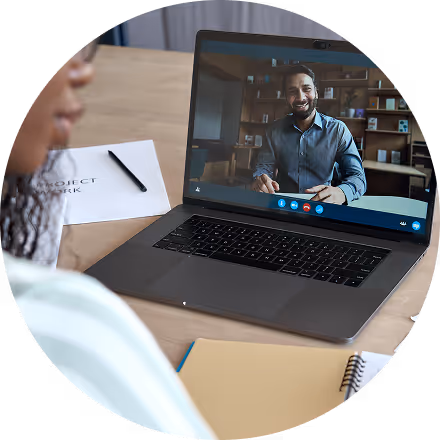 Person participating in a video call with a smiling man displayed on a laptop screen.