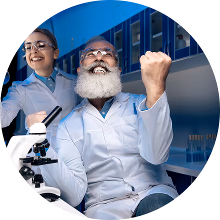 Two scientists in lab coats and safety glasses celebrating a successful experiment near a microscope in a laboratory.