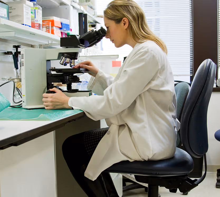 Female scientist in a white lab coat looking through a microscope in a laboratory.