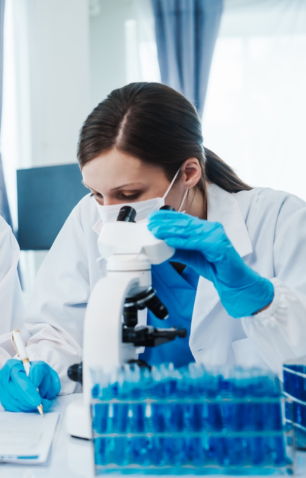 Scientist wearing a mask and blue gloves looking through a microscope in a laboratory.