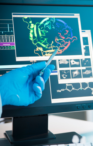 Gloved hand holding a pen pointing at a colorful 3D molecular structure on a computer screen.