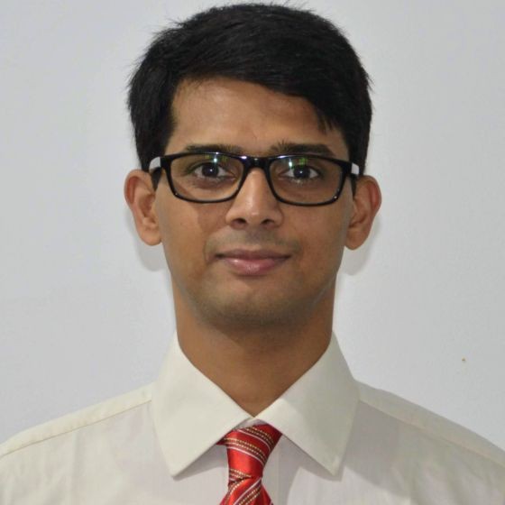 Portrait of a young man with short black hair, wearing black glasses, a white shirt, and a red striped tie, against a plain light background.