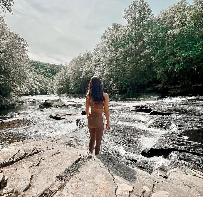 woman walking on a rocky path surrounded by trees and mountains