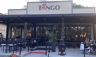 The modern exterior and covered outdoor patio of the upscale TANGO restaurant, featuring fire pits and large windows, representing the excellent food and refined atmosphere.