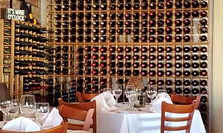 The cozy interior of an Italian eatery with dining tables set in front of floor-to-ceiling wooden wine racks, representing the relaxed atmosphere for traditional pasta and comfort meals.