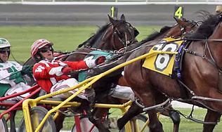 A close-up action shot of horses and drivers competing in a harness race, representing the historic harness-racing track and entertainment venue with simulcast betting.
