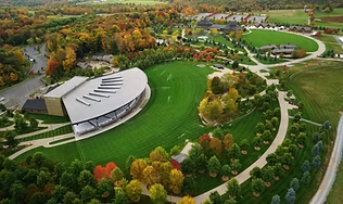 Aerial view of the iconic, crescent-shaped open-air pavilion and its vast green lawn seating area, representing the top Catskills concert venue for major tours, festivals, and summer performances.