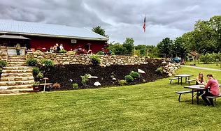 A scenic view of the Hudson Valley winery's outdoor patio and lawn, featuring a stone retaining wall and picnic tables, highlighting the perfect setting for guided wine tastings and enjoying vineyard views.