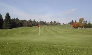 A view of the well-manicured, rolling green fairway and red flag on the championship-style Catskills golf course, highlighting the challenging par-3s and scenic lake views.