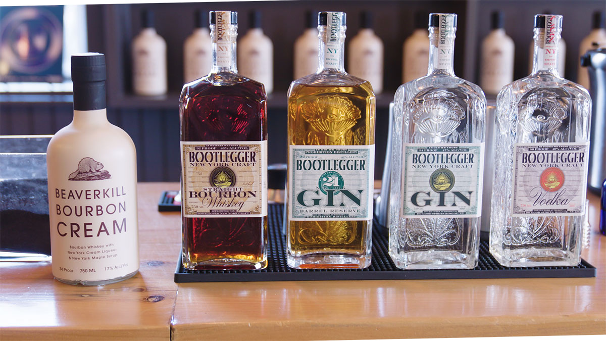 A lineup of locally distilled craft spirits, including Bootlegger Whiskey, Gin, Vodka, and Beaverkill Bourbon Cream, highlighting the variety of products available for tastings and cocktails at the Roscoe distillery.
