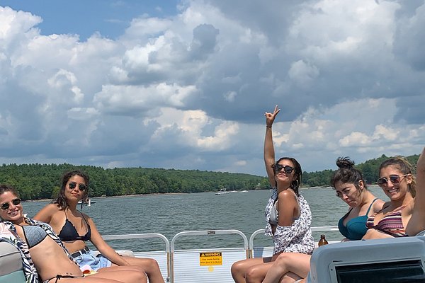 A group of friends relaxing on a pontoon boat on the calm waters of Kiamasha Lake, surrounded by green forest, illustrating the perfect spot for paddling and relaxed outdoor time.