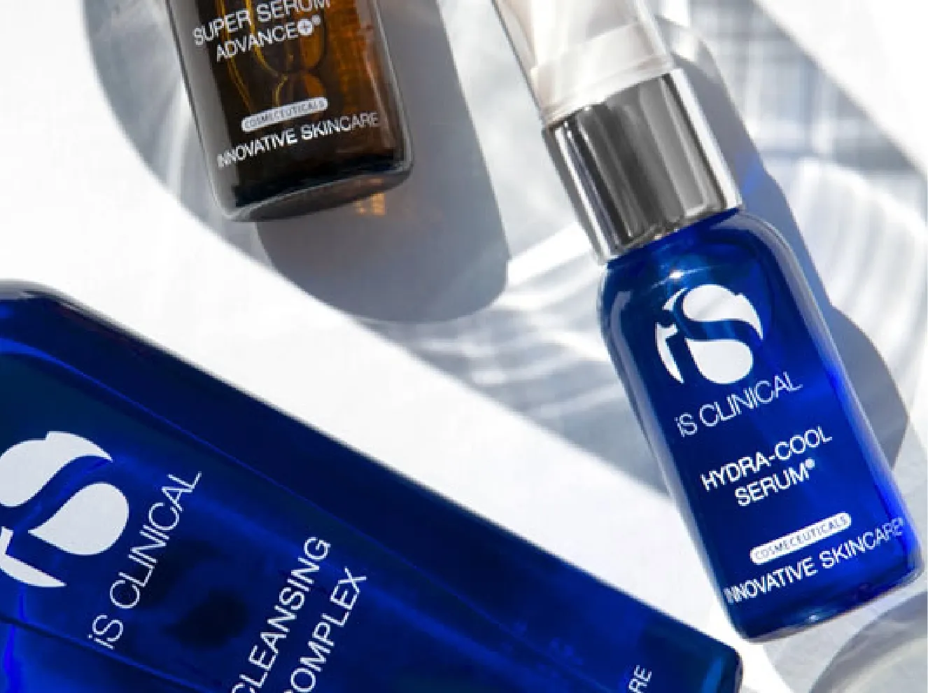 Three IS Clinical skincare products: Cleansing Complex, Super Serum Advance+, and Hydra-Cool Serum, displayed on a white surface with natural light and shadows. at Becker Cosmetic featuring Medical-Grade Skincare services