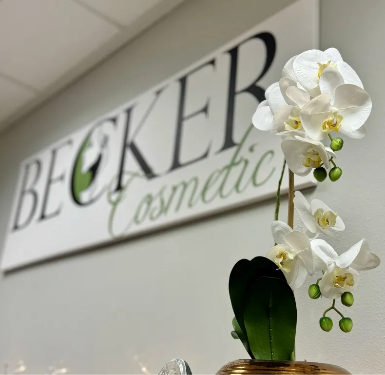 Becker Cosmetic logo sign on a wall with a white orchid plant in the foreground at Becker Cosmetic featuring cosmetic treatment services