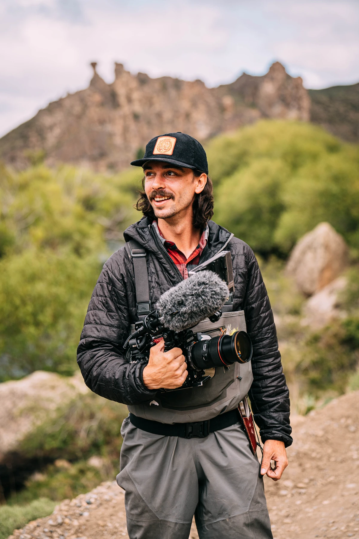Man wearing camo hoodie and cap operating a professional RED Dragon video camera outdoors.