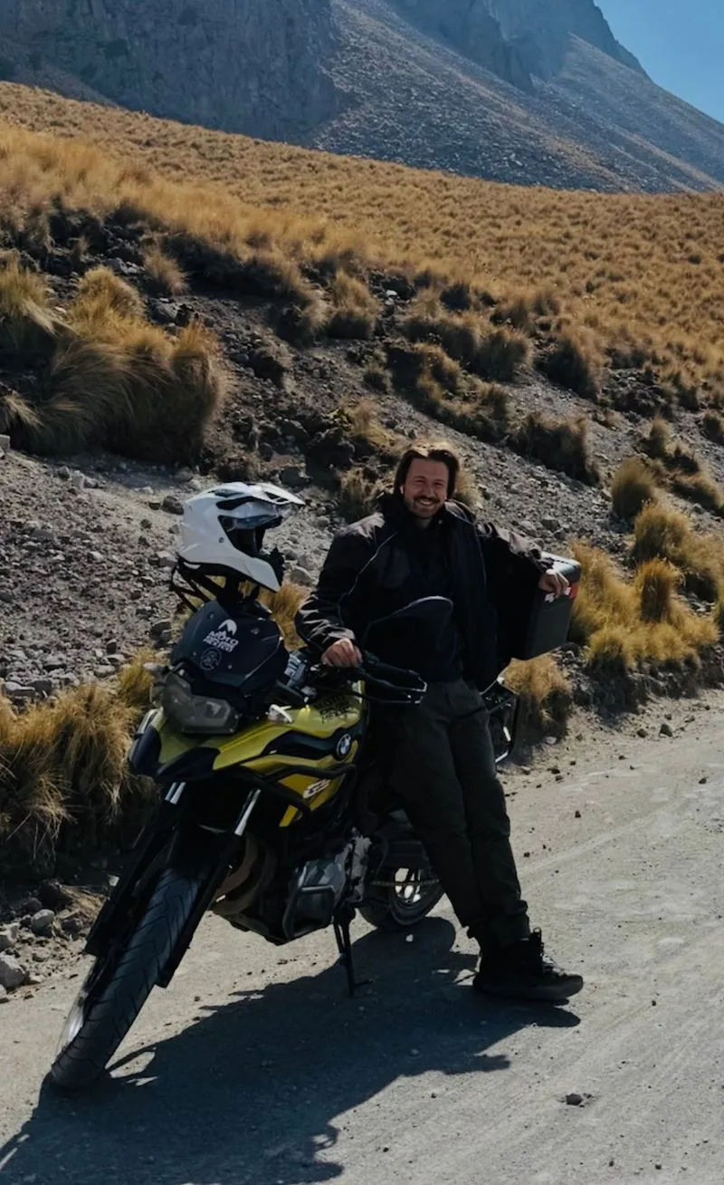 Middle-aged person wearing glasses, a Patagonia cap, and a grey button-up shirt, sitting with hands clasped in a room with bookshelves.