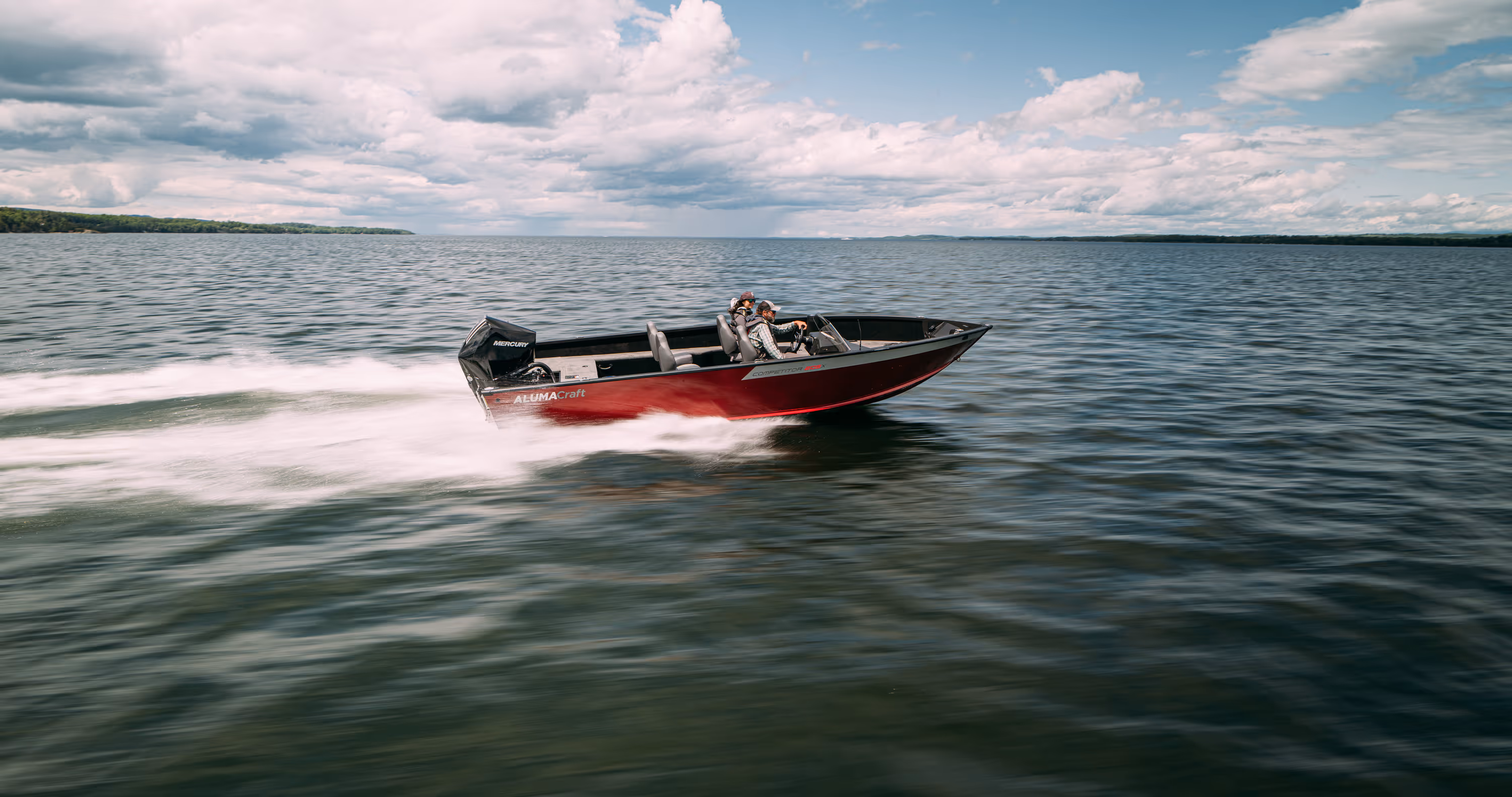 Three motorboats speeding on a lake with forested shoreline under a partly cloudy sky.